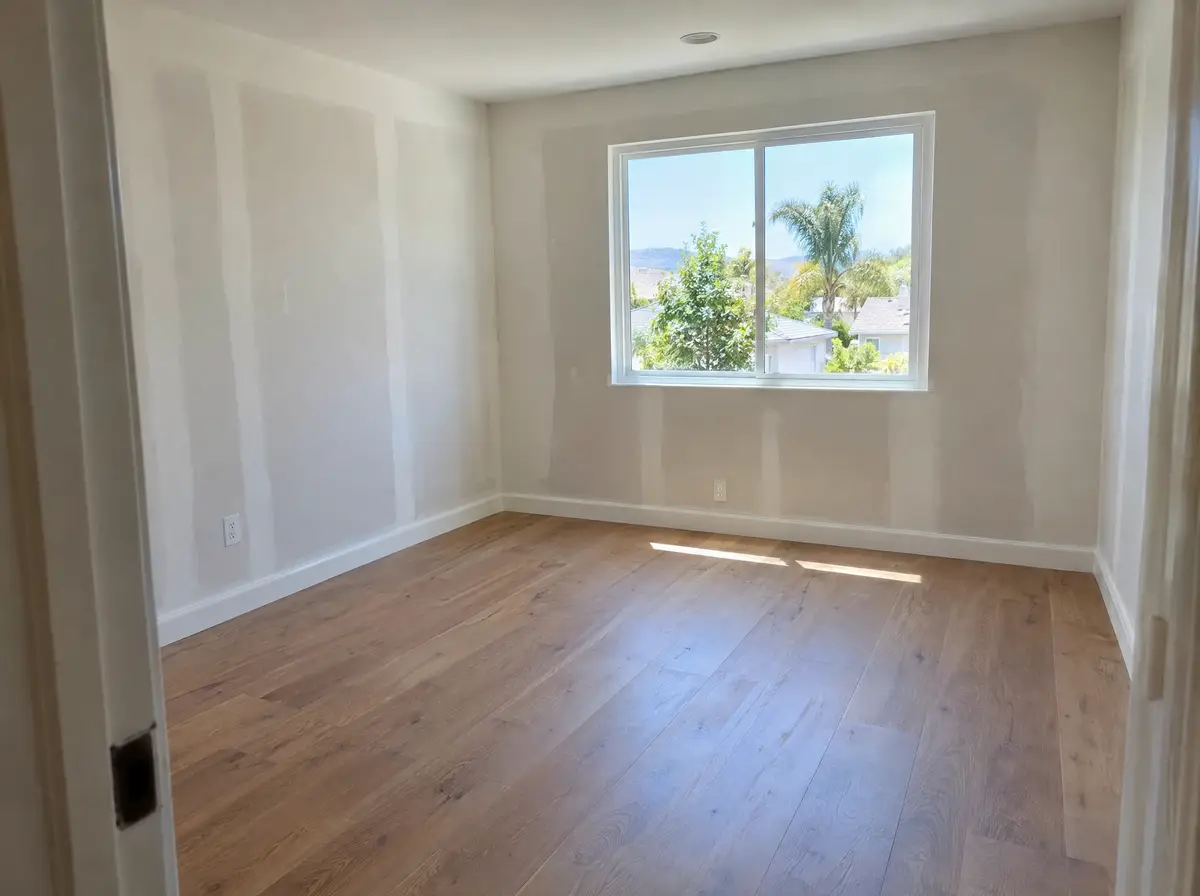 Inside a new room addition with fresh drywall, a wood floor matched to the existing hallway and a new window