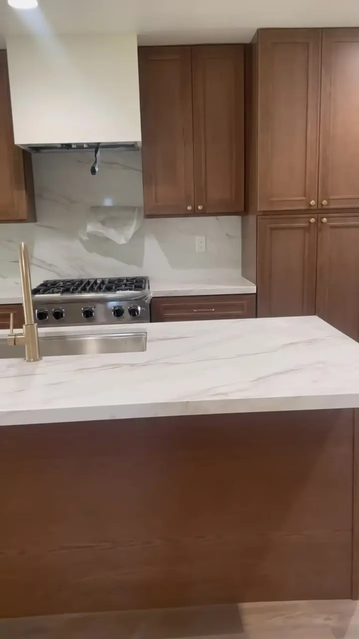 Home addition with a new primary suite in Fontana, CA: kitchen with walnut cabinets and a marble-look quartz island