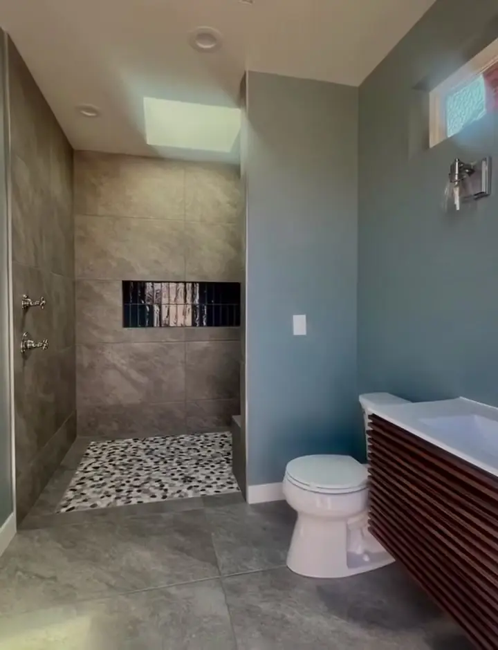 Outdoor bathroom with a pebble shower floor and a fluted wood vanity